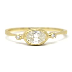 a yellow gold ring with an oval cut diamond in the center and three small diamonds on each side