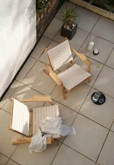 two wooden chairs sitting on top of a tiled floor next to a potted plant