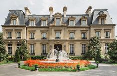 a large building with a fountain in front of it and lots of flowers around the perimeter