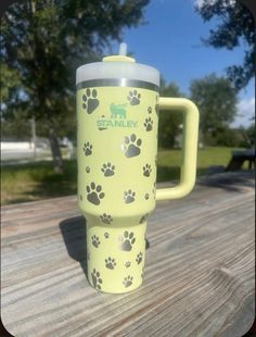 a yellow coffee cup with paw prints on it sitting on a wooden table next to trees