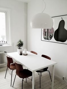 a white dining table with four chairs and a plant on the top, in front of a window