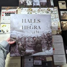 a person holding up a book on top of a table covered in cards and other items