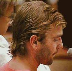 a close up of a man with long hair and glasses looking at something in his hand