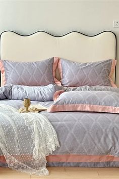 a bed with pink and grey comforters on top of it next to a white headboard