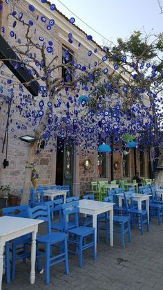 an outdoor dining area with blue and green chairs, tables and umbrellas hanging from the ceiling