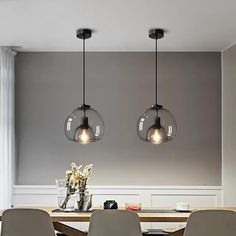 three lights hanging over a dining room table with four chairs and a vase on it