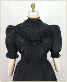 Poly Bengaline. Color: Black. Fine ribbed poly bengaline fabric. Designed with black lace front yoke and wide pleated satin and gathered scalloped lace trim. Lace trim on stand up collar, blouse front and edge of pleated short sleeves. Button back closure. Dry clean. Matching skirt sold separately. Black satin jacquard belt sold separately. Circa 1890-1905. Made in U.S.A. Sizes: SM, MED, LG & XLG.   Blouses ordered by bust measurement, inches: BUST         SIZES 32" - 34"   SMALL 35" - 39"   MEDIUM 40" - 44"   LARGE 45" - 49"   XLARGE Blouses ordered by bust measurement, centimeters: SMALL       81 cm - 86 cm MEDIUM    88.9 cm - 99 cm LARGE      101.6 cm - 111.76 cm XLARGE    114 cm - 124.46 cm HOW TO MEASURE TO DETERMINE YOUR SIZE: BUST: Measure the fullest part of your bust, we add the f Fitted Gothic Victorian Dress With Lace Trim, Black Gothic Blouse For Formal Occasions, Classic Black Satin Blouse, Fitted Black Blouse With Doll Collar, Black Doll Collar Blouse For Party, Black Gothic Short Sleeve Blouse, Elegant Black Blouse With Stand Collar, Elegant Victorian Dress With Ruffles And Doll Collar, Elegant Fitted Victorian Dress With Lace Patchwork