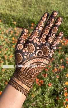 henna tattoo on the palm of someone's hand with flowers in the background