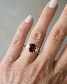 a woman's hand with a ring on it that has a red stone in the middle