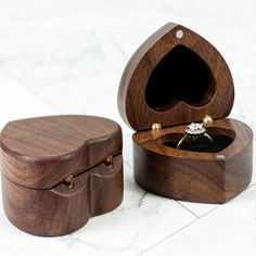 an open wooden box with a ring inside on a white marble countertop next to a small black diamond in it