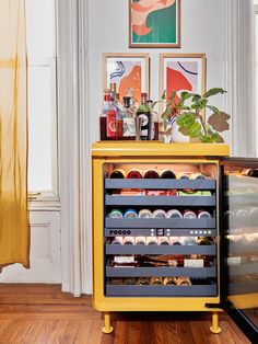 a yellow cabinet with drinks in it on the floor next to a window and potted plant