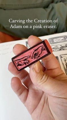 a person is holding a pink eraser in their left hand with the words carving the creation of adam on a pink eraser