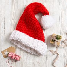 a red knitted santa hat next to presents on a white wooden table with ribbon