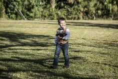 a young boy standing in the grass holding a stuffed animal