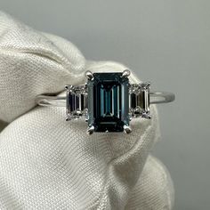 an emerald and diamond three stone ring on a white cloth with two diamonds around it