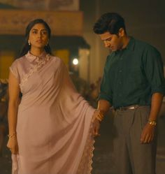 a man standing next to a woman in a pink sari and holding the hand of her