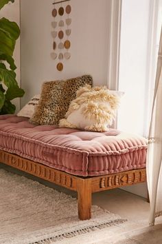 a pink daybed with pillows on it in front of a large potted plant