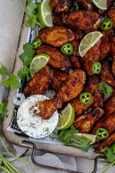 chicken wings with limes and sour cream sauce on a tray next to some cut up cilantro