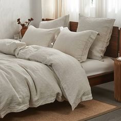 a bed with white linens and pillows in a room next to a window filled with curtains