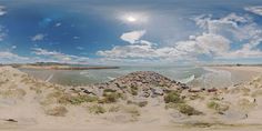 the fish eye lens is showing sand dunes and water in the distance, with blue sky and white clouds