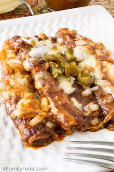 a white plate topped with lasagna covered in cheese and peppers next to a fork