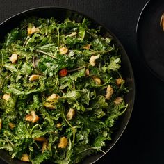 a salad in a black bowl next to a glass of wine on a dark table