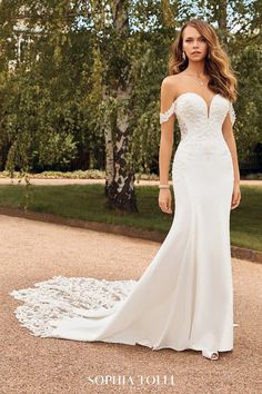 a woman in a white wedding dress standing on a path with trees and grass behind her