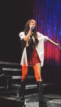 a woman in tights and boots is singing on stage with her arms out to the side