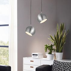 three lights hanging from the ceiling above a white dresser and chair in a living room