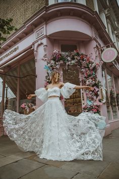 a woman in a white dress is standing on the sidewalk with her arms outstretched and hands out