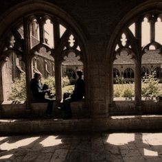 two people sitting on a bench in an old building with arches and sun shining through the windows