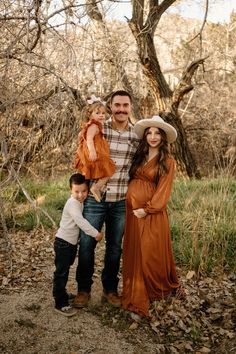 a man, woman and two children posing for a photo in the woods with leaves on the ground