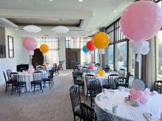 tables and chairs are set up for an event with balloons hanging from the ceiling above them