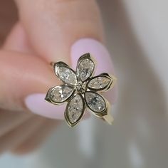 a woman's hand holding a gold ring with white stones on it and a flower shaped diamond in the middle