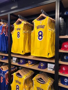 several yellow jerseys are on display in a store with hats and baseball caps behind them