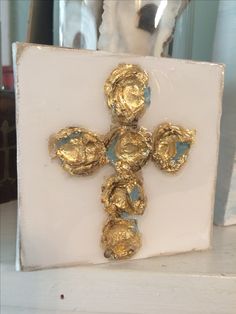 a cross made out of gold leafy material on a white surface with a vase in the background