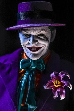 a man dressed as the joker holding a purple flower in his left hand and wearing a top hat