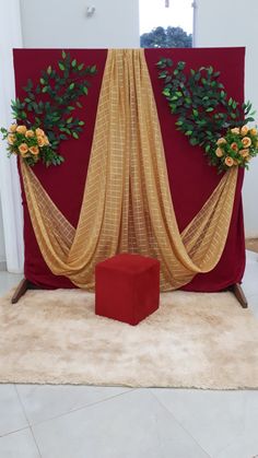 an arrangement of flowers and greenery is displayed on a red backdrop with gold drapes