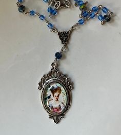 "Marie Antoinette Coeffure Cameo Glass Necklace with Blue Crystal glass bead and silver tone chain. The cameo is an art image set under glass in a vintage style antique silver bezel. The pendant length is 2\"s long and the pendant is 1 1/4\" wide. It hangs from a pressed silver tone antiqued silver Victorian style connector. The necklace is adjustable from up to 19\"s.  Will come gift boxed and will make a lovely gift." Artistic Blue Beaded Necklace, Artistic Blue Beaded Jewelry, Vintage Blue Necklace With Silver Beads, Vintage Blue Beaded Necklace Gift, Blue Crystal Beads, Victorian Pendants, Cameo Necklace, Marie Antoinette, Glass Necklace