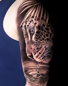 a woman's arm with a leopard tattoo on it and water in the foreground