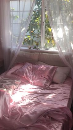 an unmade bed in front of a window with sheer curtains