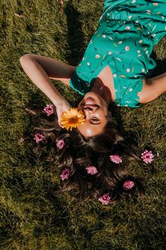 a woman laying on the grass with a flower in her hair and wearing a green dress