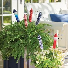 a potted plant with some patriotic flags in it on the front porch, next to a white bench