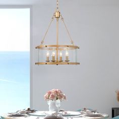 a chandelier hanging over a dining room table with flowers in the vase on it