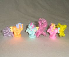 five little pony toys are lined up on a table top, one is pink and the other is yellow