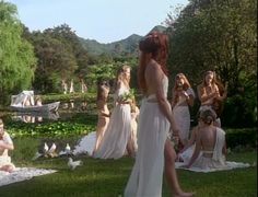 a woman in a white dress standing next to other women and birds on the grass