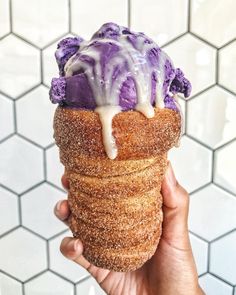 a hand holding an ice cream cone with purple icing