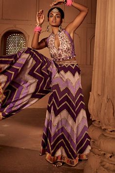 Lilac and purple sharara featuring geometrical prints. Comes with coordinated, intricately embroidered padded blouse with heavy tassels and doris at back.
Components: 2
Pattern: Printed
Type Of Work: Chevron Patterns
Neckline: Mandarin Notched
Sleeve Type: Sleeveless
Fabric: Raw Silk
Color: Purple
Other Details: 
Backless with tassel tie-up
Length:
Blouse: 14 inches
Sharara: 44 inches
Model height: 5ft 8inches, wearing size S
Note: All the jewellery worn by the model is not for sale
Occasion: De Bohemian Silk Sharara For Reception, Silk Bohemian Sharara For Party, Bohemian Silk Sharara For Party, Bohemian Saree Sets For Reception, Fitted Bohemian Dress With Gota Work, Purple Sleeveless Festive Sets, Sleeveless Purple Party Set, Purple Lehenga With Gota Work, Purple Gota Work Lehenga