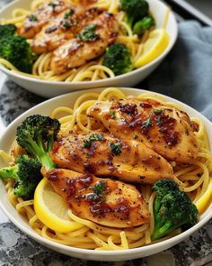 two white bowls filled with chicken and lemon pasta on top of a marble countertop