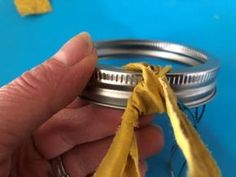 a person holding a yellow piece of fabric in front of a metal jar with some thread on it